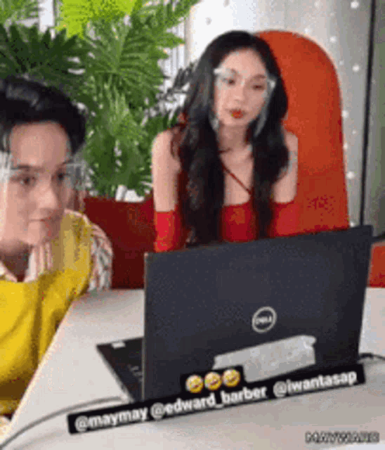 a man and a woman are sitting at a table looking at a dell laptop .