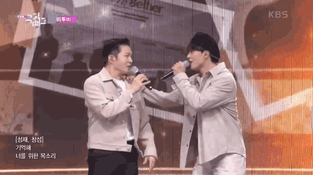 two men singing into microphones on a stage with a kbs logo in the corner