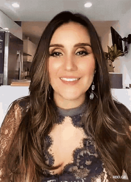 a woman wearing a lace top and earrings smiles in a kitchen