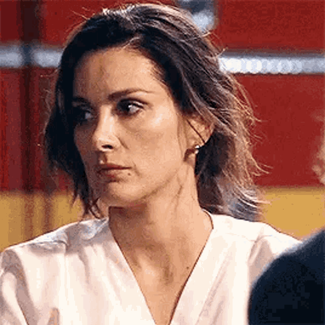 a woman in a white shirt is making a funny face while sitting in front of a red wall .
