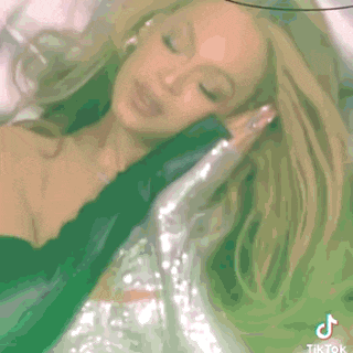 a woman in a green dress is laying on a bed with her eyes closed and her hair in her hand .