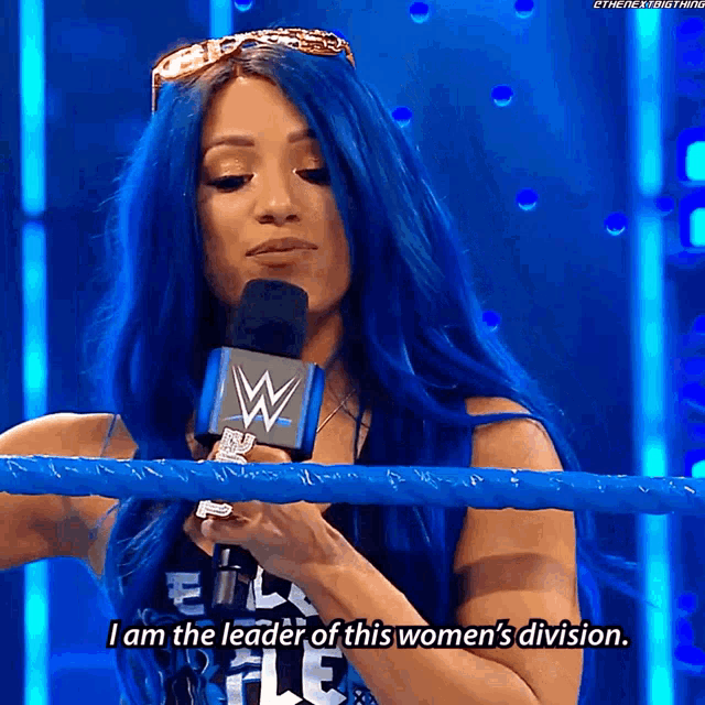 a woman with blue hair is talking into a microphone and says i am the leader of this women 's division
