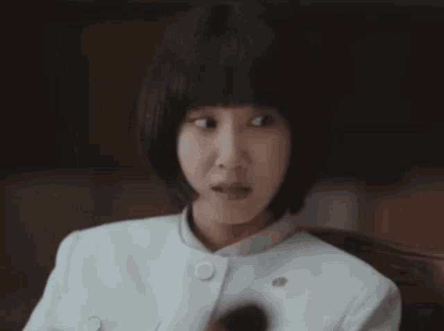 a woman with short hair and a white jacket is sitting in a chair and making a funny face .