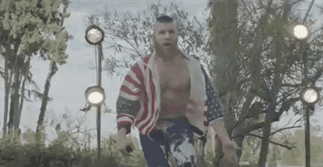 a man without a shirt is wearing an american flag jacket and jeans .
