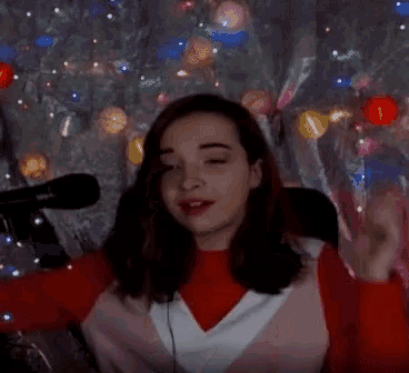 a woman is sitting in front of a microphone with christmas lights in the background .