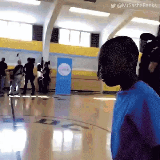 a boy in a blue shirt is standing in a gym with a sign that says ' mrsashabanks ' on it