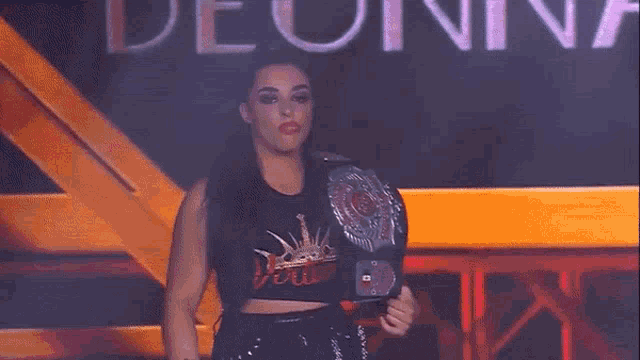 a female wrestler is holding a championship belt in her hand .