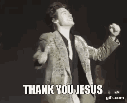 harry styles is singing into a microphone and saying `` thank you jesus '' while holding his fist in the air .
