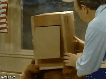 a man in a blue shirt is holding a cardboard box in front of his face .