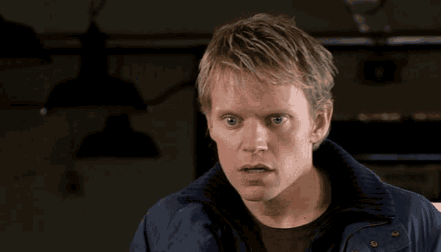 a man in a blue jacket looks at the camera with a serious look on his face