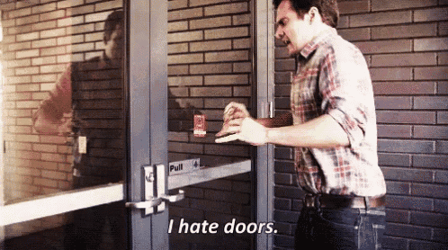 a man in a plaid shirt is standing in front of a door that says " i hate doors "