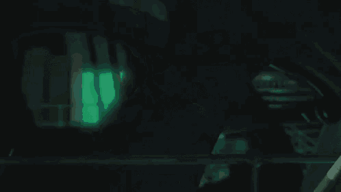 a man wearing a mask and a hat is standing in the dark with a green light behind him