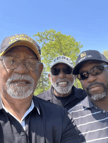 three men are posing for a picture and one of them is wearing a hat that says momt38
