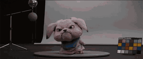 a pink stuffed animal with a blue scarf around its neck is standing on a table next to a color checker