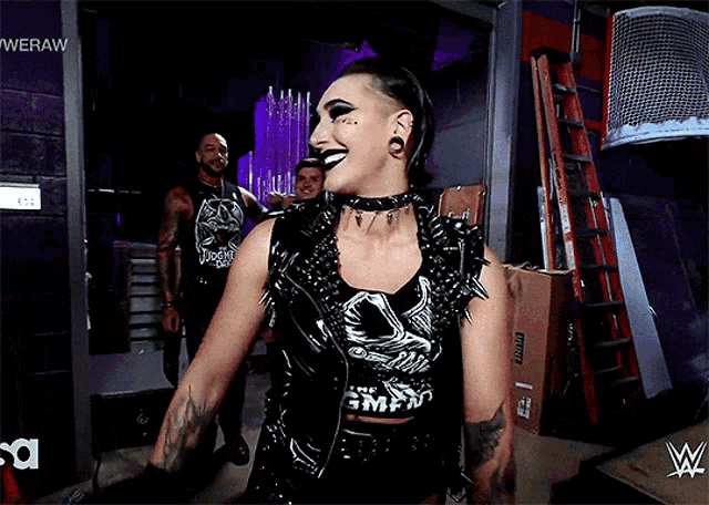 a woman in a black and white outfit is smiling in front of a sign that says wweraw
