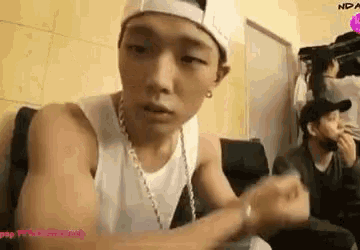 a young man wearing a hat and a white tank top is sitting in a room .