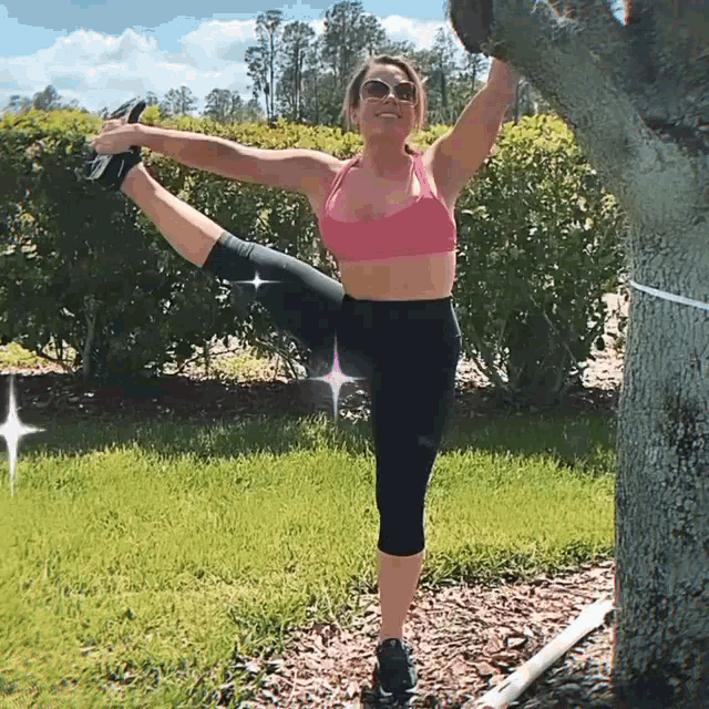 a woman in a pink top and black leggings is stretching her leg