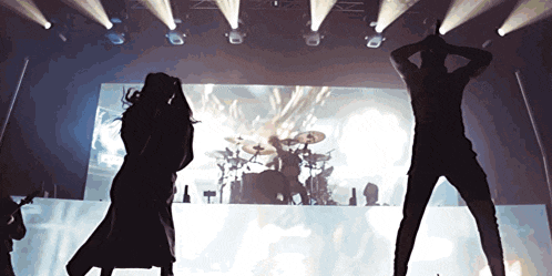a man and a woman are dancing on a stage with a drum set in the background