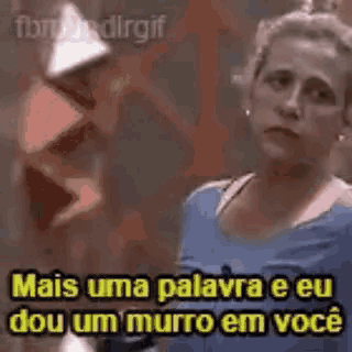 a woman in a blue shirt is standing in front of a wall and saying mais uma palavra e eu dou um murro em voce