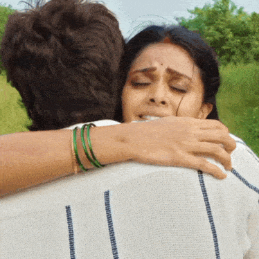 a woman with green bracelets is hugging a man in a white shirt