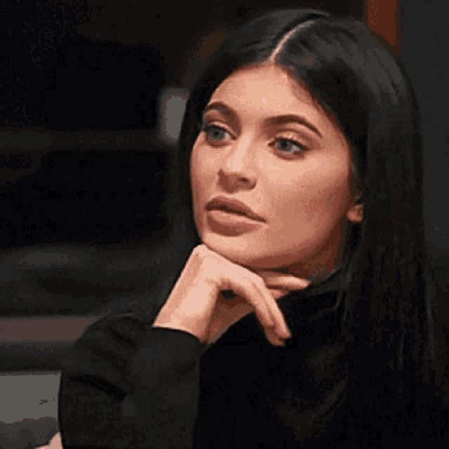 a woman in a black turtleneck is making a funny face while holding her finger to her face .