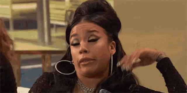 a woman wearing hoop earrings and a choker is sitting on a couch and touching her hair .