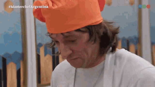 a man wearing an orange chef 's hat with the hashtag #masterchefargentina on the bottom