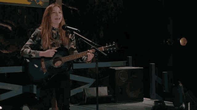 a girl singing into a microphone while holding a guitar