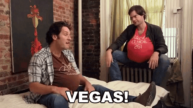 two men sitting on a bed with the word vegas written on the bottom