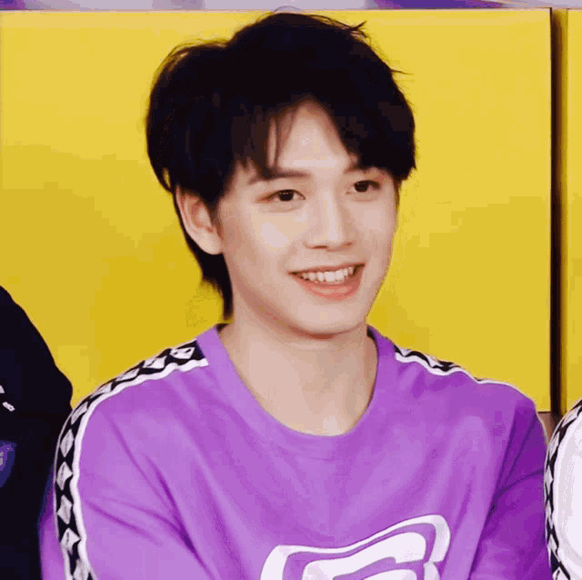 a young man wearing a purple shirt with the letter g on it smiles
