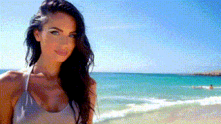 a woman in a bikini stands on a beach looking at the camera