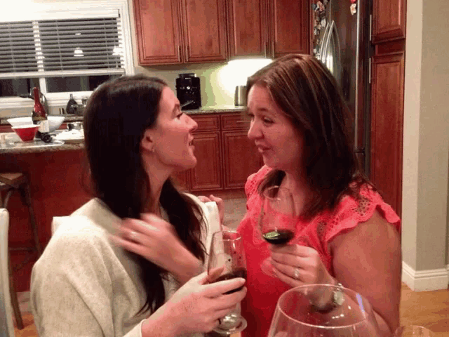 two women sitting at a table drinking wine and talking