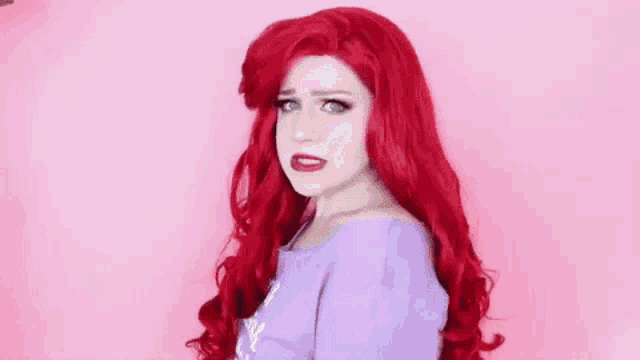 a woman with red hair is wearing a purple dress and a red wig and making a funny face .