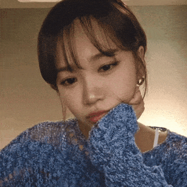 a woman in a blue sweater has her hand on her face