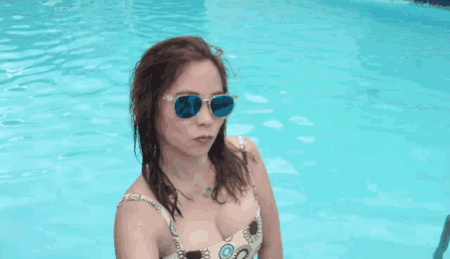 a woman in a bathing suit and sunglasses is standing in a pool
