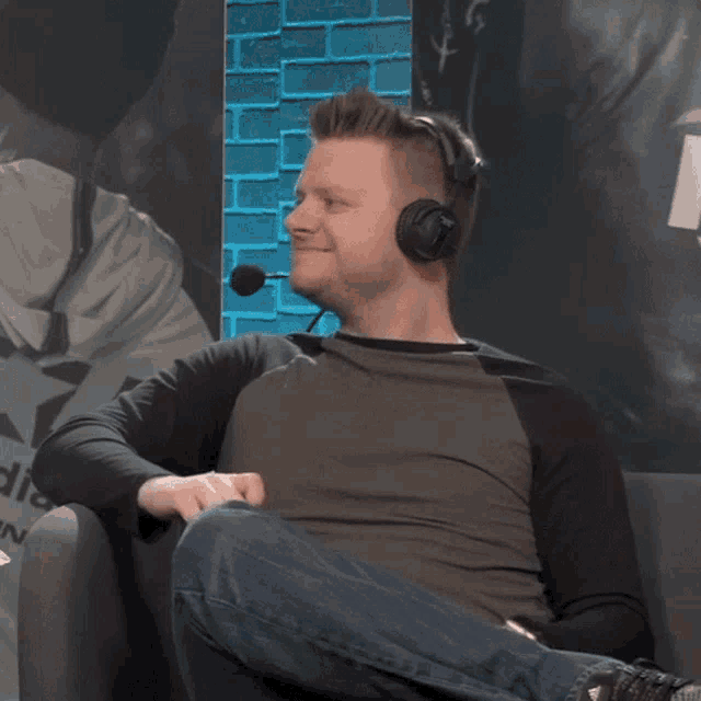 a man wearing headphones sits on a couch in front of a brick wall that says adidas