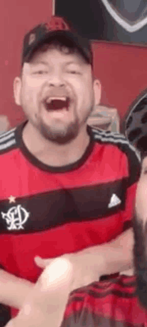 a man with a beard is wearing a red and black shirt and a black hat .