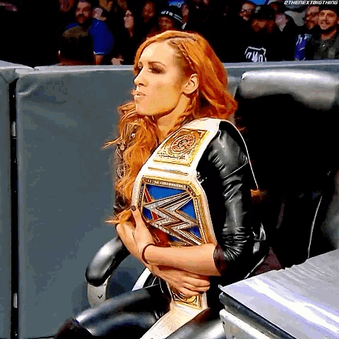 a woman with red hair is sitting in a chair holding a wrestling belt .