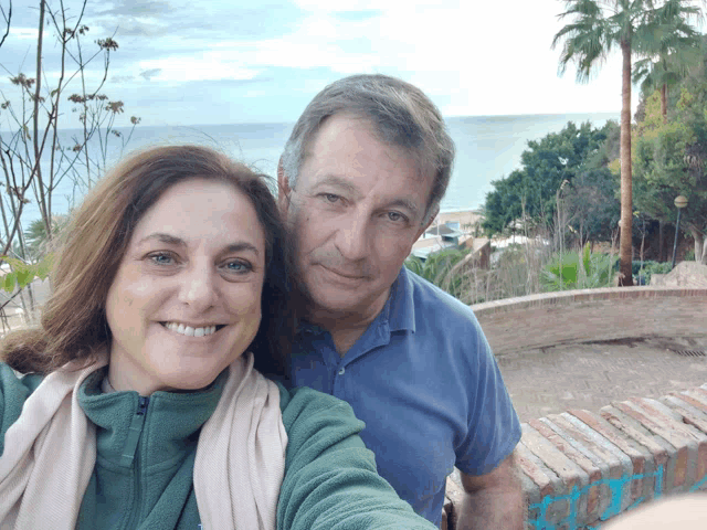 a man and a woman are posing for a selfie in front of the ocean