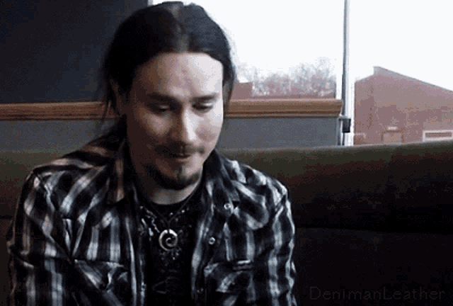 a man in a plaid shirt is sitting on a green couch with the words denimanleather below him