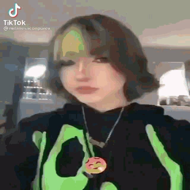 a girl with short hair is wearing a green shirt and a necklace with a smiley face pendant .