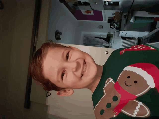 a young boy wearing a gingerbread man sweater smiles for the camera