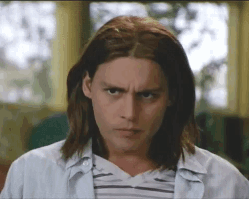 a young man with long hair and a striped shirt looks at the camera