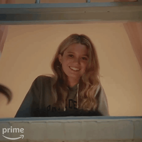 a woman is smiling while looking out of a window and wearing a sweatshirt that says pk on it .