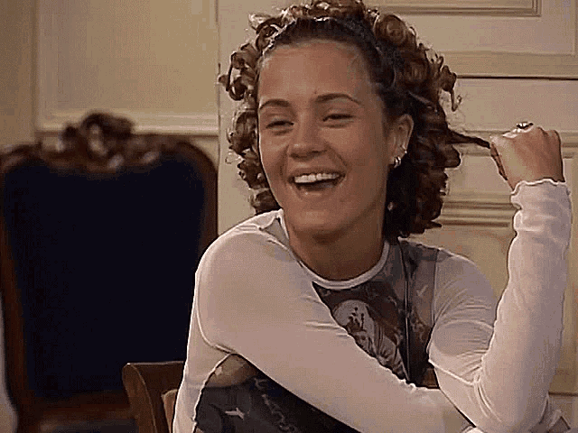 a woman with curly hair is sitting in a chair and laughing while holding her hair .