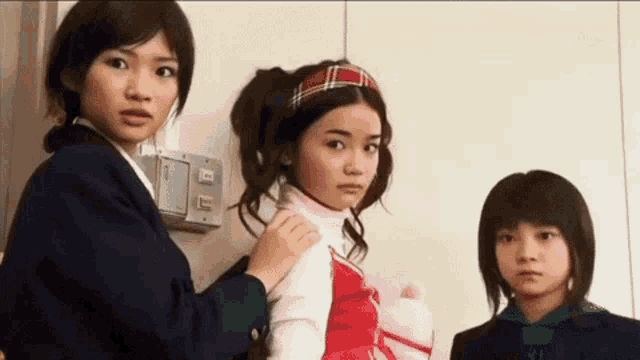 three young girls are standing next to each other and one of them is wearing a red and white outfit