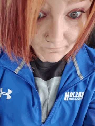 a woman is wearing a blue jacket that says holzman auto & motors
