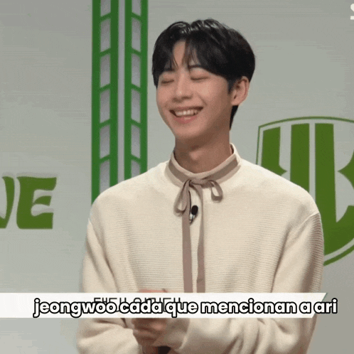a young man is smiling in front of a sign that says jeong woo cada que mencionan ari