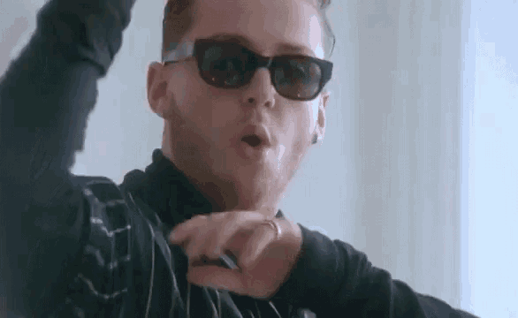 a close up of a man wearing sunglasses and a ring on his finger .