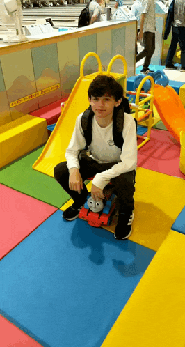 a boy sitting on a toy train in a play area